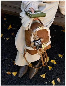 Brown suede mini backpack with white faux fur trim and cute rabbit doll charm on a park bench