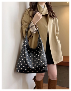 Detailed view of black leather hobo bag with silver studs worn with a trench coat