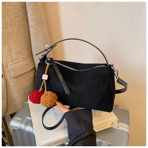 Detail of black suede hobo bag with red tassel on books and silver suitcase