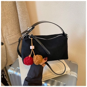 Close-up of black suede pillow bag with cherry plush charm and glossy leather handle
