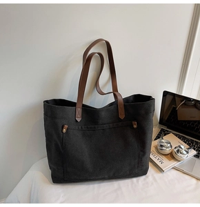 Detail of a large black canvas tote bag with brown leather handles and metal rivets