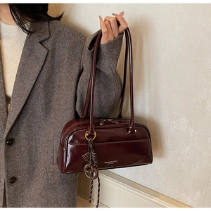 Détail du sac oreiller en cuir verni bordeaux avec logo de la marque et charme tissé
