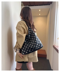 Detailed view of black rivet shoulder bag with gold studs and wide strap on model