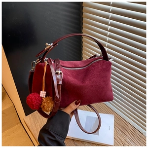 Close-up of burgundy suede pillow bag with dual-tone pompom and metal zipper detail