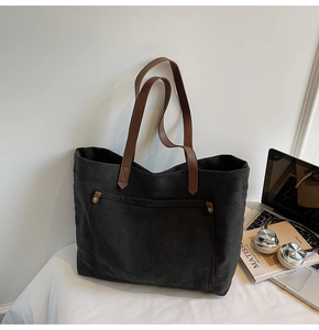 Detail of a charcoal canvas tote bag with brown leather handles and vintage rivets