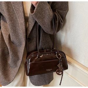 Détail d'un sac bowling en cuir verni marron foncé avec logo doré et longues anses fines