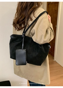 Minimalist black suede tote bag with small zipper pouch shown on person in trench coat