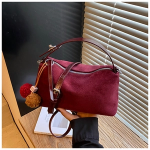Close-up of burgundy frosted suede pillow bag with plush ball charm and silver zipper