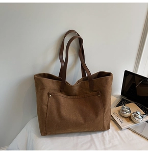 Close-up of brown suede tote bag with leather straps and metal rivets on a white desk