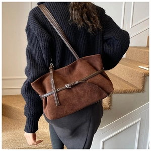 Gros plan sur un sac cabas en daim marron avec boucle argentée porté à l'épaule du mannequin