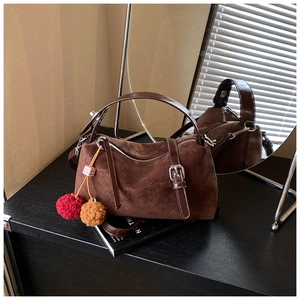 Detail of coffee brown suede handbag with plush ball charm and silver hardware on a desk