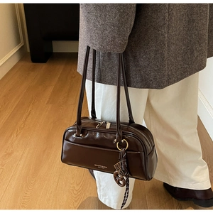 Détail d'un sac oreiller marron foncé brillant avec breloque tissée et double bandoulière