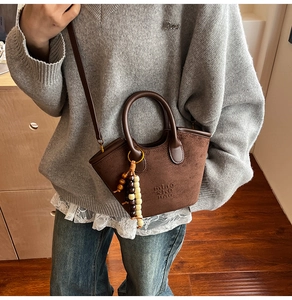 Detail of dark brown suede bucket bag with leather handles and decorative wooden beads
