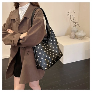 Close-up of black leather shoulder bag with silver studs on a stylish model in trench coat