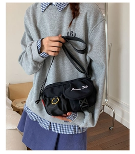 Detail of black nylon crossbody bag with flap pockets and yellow ring buckle on model