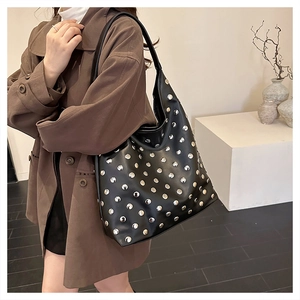 Close-up of black leather hobo bag with silver rivets worn by a model in a trench coat