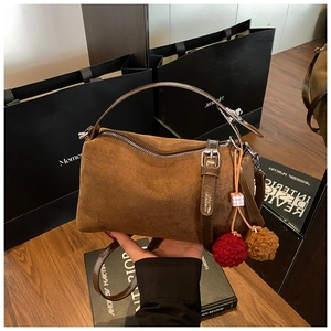 Detail of brown suede pillow bag featuring leather handles and plush charm accessories