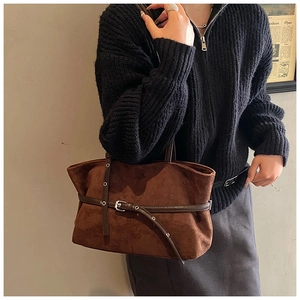 Detailed close-up of brown suede tote bag with decorative buckle on dark knitwear