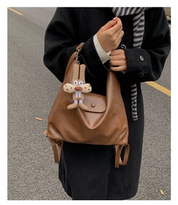 Detail of caramel brown leather backpack with magnetic flap and cute plush rabbit charm