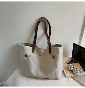 Detail of canvas tote bag showing front pocket and brown leather shoulder straps
