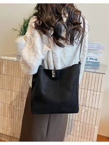 Detail of black matte suede bucket bag with silver clasp worn on a white sweater