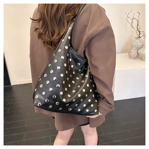 Detail of black hobo bag with silver metal studs worn on a shoulder over a brown coat