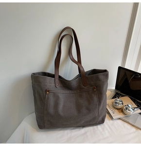 Detail of canvas tote bag with brown leather straps, metal rivets and front pocket