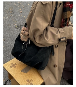 Détail d'un grand sac noir avec breloque ours porté avec un trench-coat d'automne