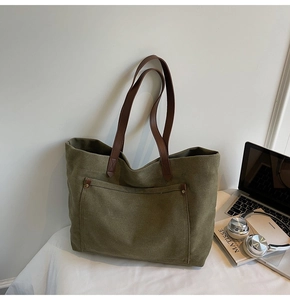 Detail of olive green canvas tote bag with brown leather straps and metal rivets