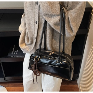 Détail du sac polochon noir en cuir verni avec logo doré et pendentif tressé élégant