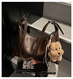 Detail of dark brown retro leather underarm bag with vertical stitching and plush dog charm