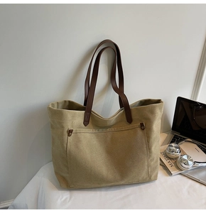 Detail of khaki canvas tote bag with brown leather straps and front pocket with rivets