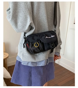 Detail of black utility crossbody bag showing modern embroidery and yellow ring accent