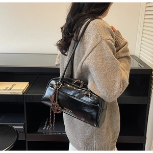 Détail d'un sac oreiller en cuir noir brillant avec fines bretelles et breloque