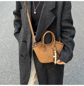Brown suede basket bag detail with vintage wooden beads and logo on wool coat background