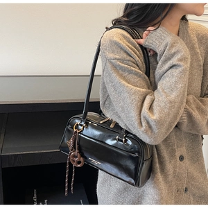 Détail d'un sac oreiller noir brillant avec fines bretelles et breloque tressée