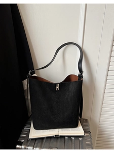 Detail of matte black bucket bag with silver metal lock and brown lining on luggage