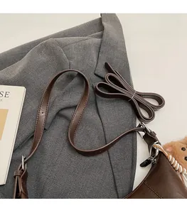 Detail of brown faux leather shoulder bag featuring a cute bear charm and adjustable strap