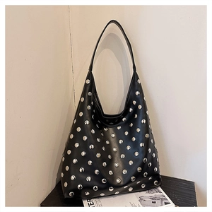 Close-up of black leather tote bag with silver studs on minimalist wall background