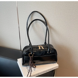 Détail du sac polochon noir brillant avec zips dorés et breloque tissée sur livres
