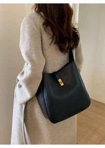 Chic black leather bucket bag with gold twist lock shown on model's shoulder in interior