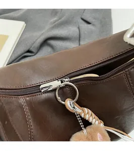 Close-up of brown leather bag featuring silver zipper and plush pom-pom charm detail