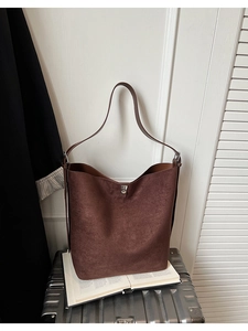 Detail shot of large brown matte bucket bag resting on an open book and silver suitcase