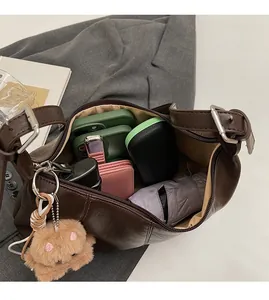 Spacious interior of brown crescent bag holding phone, umbrella, and makeup items
