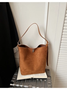 Detail of a brown suede bucket bag with a silver twist lock on a lifestyle background