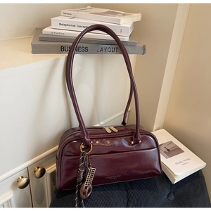 Détail du sac à main en cuir verni bordeaux avec double fermeture et pendentif boulier