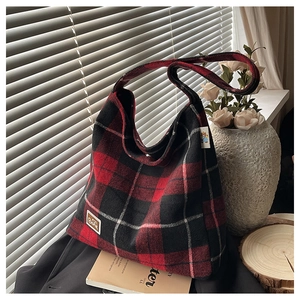 Macro detail of red and black plaid wool tote bag with leather bear patch and soft texture