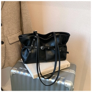 Détail d'un cabas en similicuir noir avec sangles à œillets sur une valise argentée