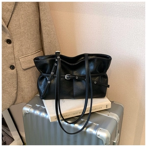 Détail du sac cabas en daim noir avec boucles métalliques sur une valise argentée