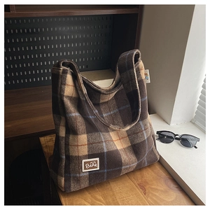 Detailed macro view of brown plaid woolen tote bag featuring a stitched BEAR square label